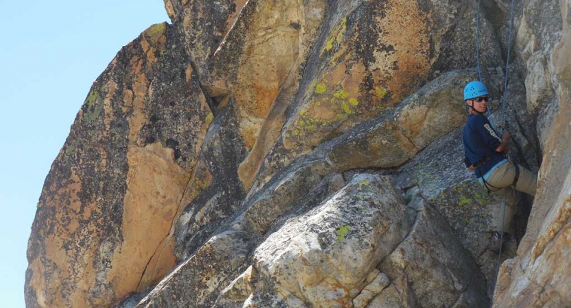 A person wearing safety gear is secured by ropes as they climb a rock wall. 